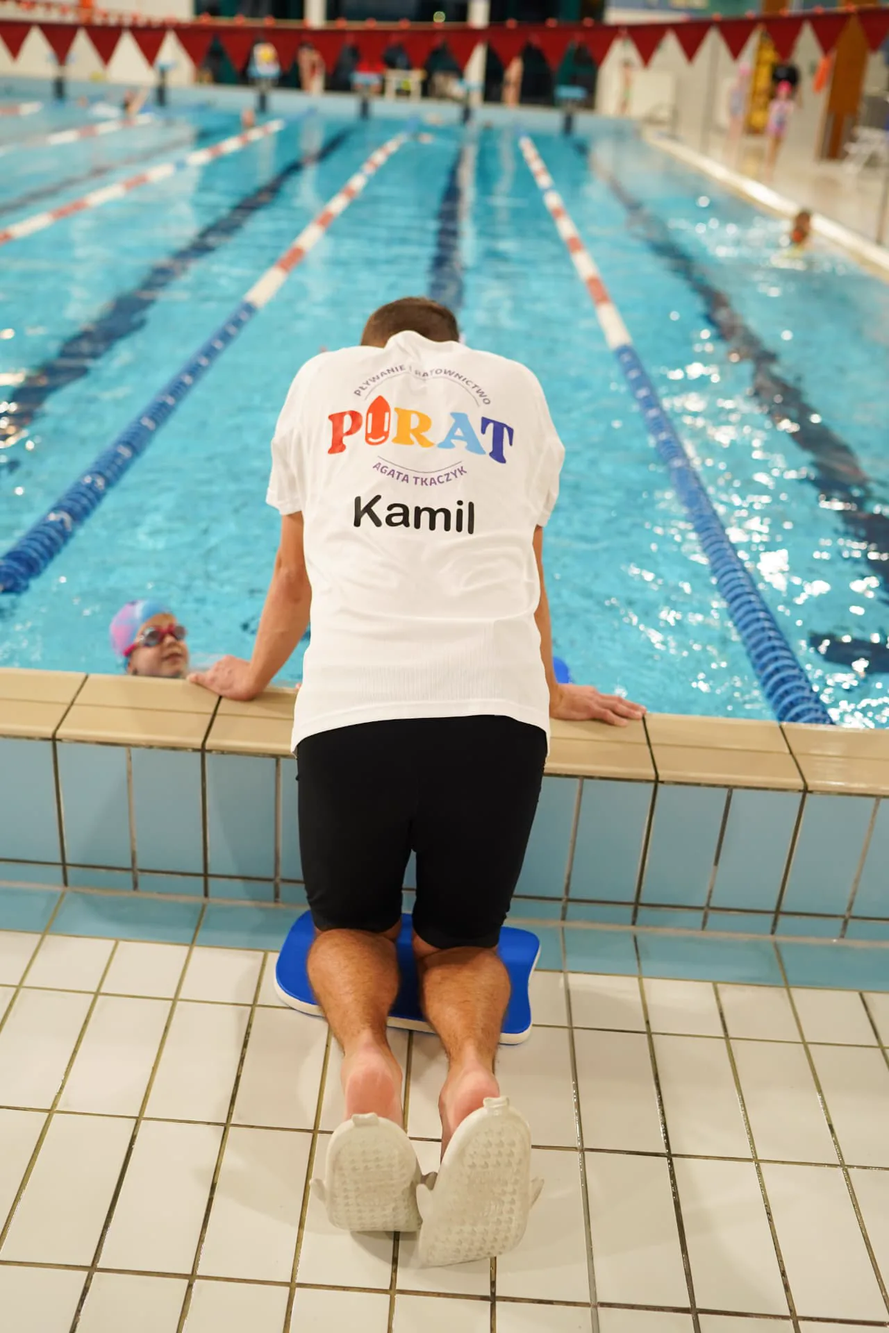 Instruktor Kamil przy torze pływackim korygujący technikę dziecka